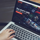 A person with a macbook laptop stares at the main Netflix splash screen with their hands hovering over the keyboard.